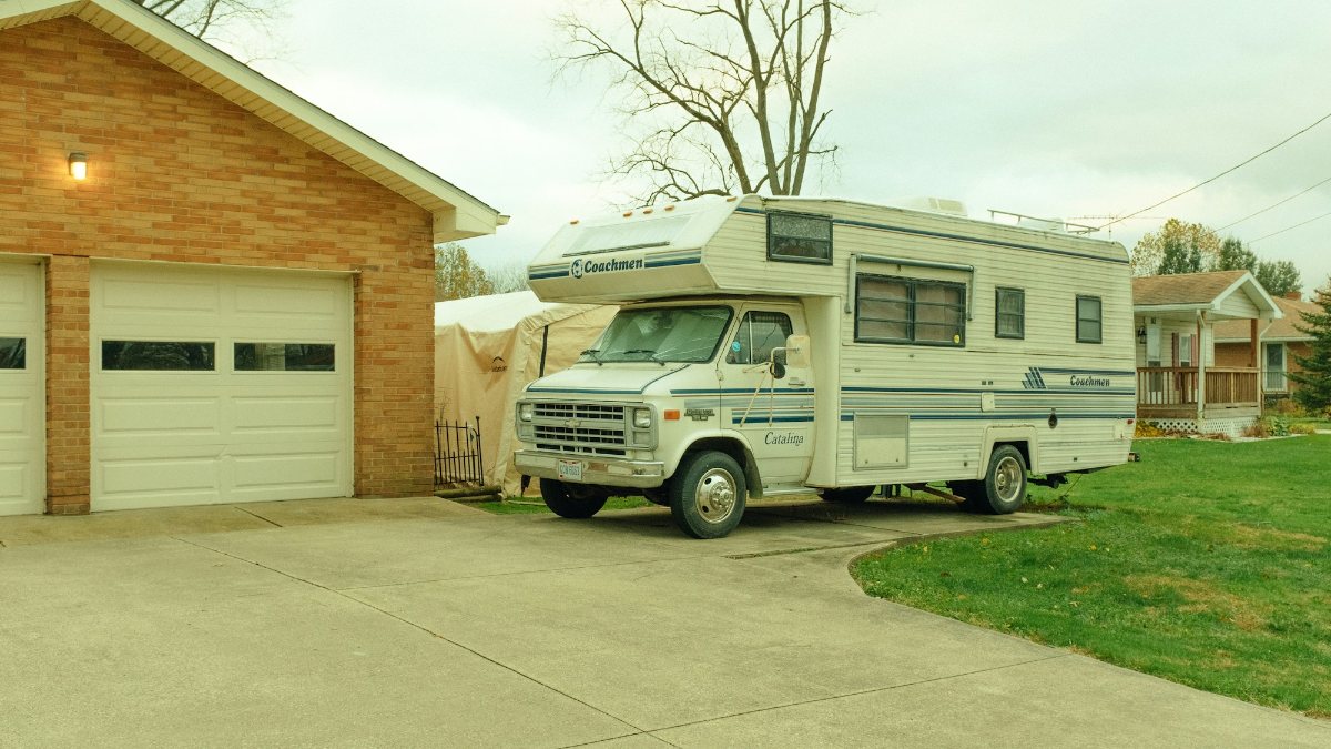Class C motorhome parked on a driveway beside a house garage
