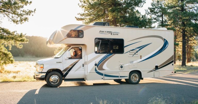 First time RV driving: a Class C motorhome driving on a paved road through pine trees