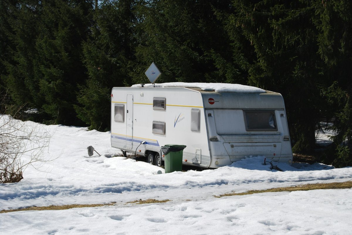 Travel trailer parked in snow beside a forest in winter